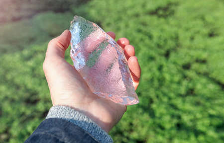 Piece of ice in a man's hand on a background of green grass with blurred focus. Concept of the onset...