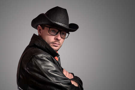 Unshaven young man with glasses, a hat and a black cloak. Cowboy portrait of a man, western culture, style. Turned sideways.の写真素材