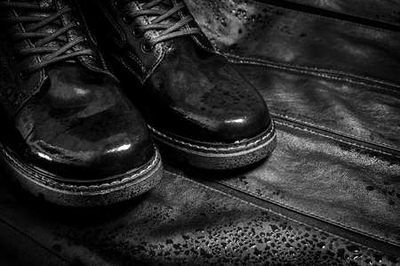 Black wet boots made of genuine leather. Men's shoes with laces with water drops. Fashionable style. On a dark contrasting leather background. Black and white image.の写真素材