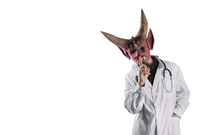 Not an honest doctor in a devil mask on a white isolated background. Hand gesture. Silence concept. Deception in treatment. Halloween.の写真素材