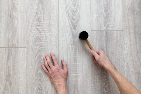Concept of noisy work. Construction work on laying laminate on the floor or wall. Knocking, blows with a rubber mallet. Silence breaking. Percussion instrument in a male hand.の写真素材