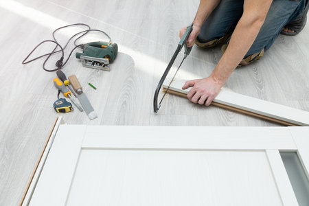 Worker assembles a door frame by cutting off the part with a hand saw. Repair and decoration of apartments. Installation and installation of interior doors. Carpentry work and tools.の写真素材