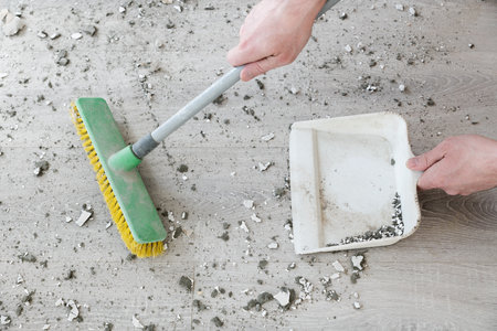Cleaning of dusty and dirty premises after repair work. Pieces of concrete and plaster are swept with a brush into the scoop. The concept of heavy floor pollutionの写真素材
