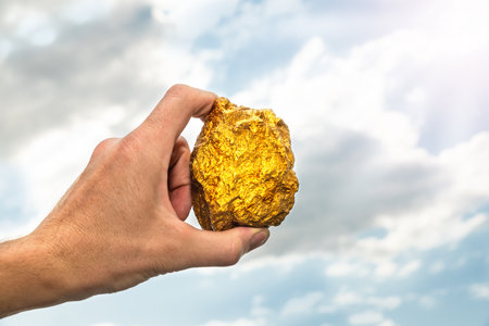 Gold nugget in a man's hand raised to the sky. The concept of wealth and success in the financial sector. Treasure, investment. Mining industry.の写真素材