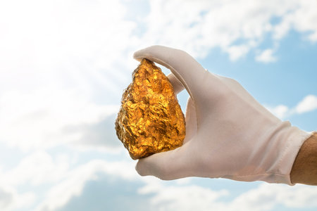 Golden nugget in a man's hand in a white glove raised to the sky. The concept of wealth and success in the financial sector. Treasures, investments. Mining industry.の写真素材
