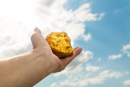 Gold nugget in a man's hand raised to the sky. The concept of wealth and success in the financial sector. Treasure, investment. Mining industry.の写真素材