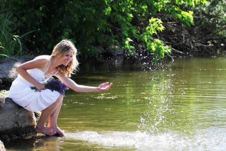 young woman sprinkles water near the lakeの写真素材