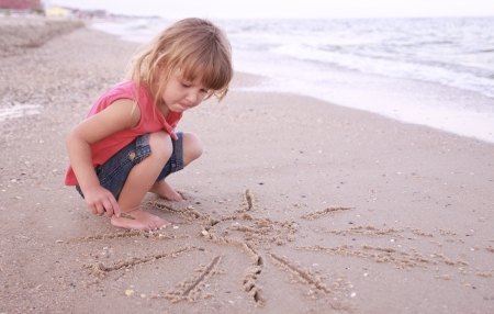 Little girl draws a sun in the sand on the beachの写真素材