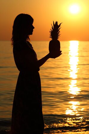 girls silhouette by the sea on summer with a pineappleの写真素材