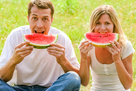 happy couple in love eating watermelon outdoors in summer parkの写真素材