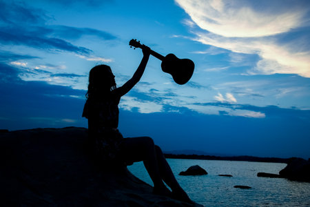 happy girl with ukulele by the sea on nature silhouette backgroundの写真素材