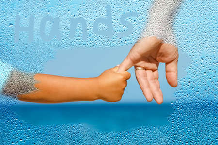 Dad holds the hand of a child by the Greek sea through a window with drops on the shore backgroundの写真素材