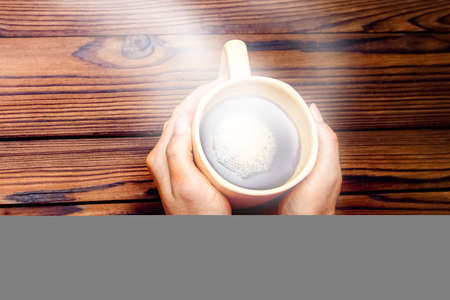 Female hands holding cup of coffee on wooden backgroundの写真素材