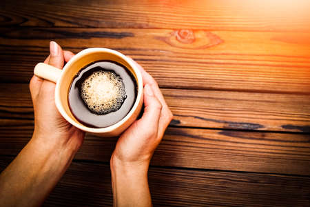 Female hands holding cup of coffee on wooden backgroundの写真素材