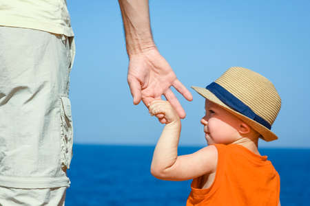 Hands of child and parent on vacation by the sea background.の写真素材