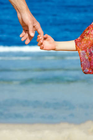 Hands of child and parent on vacation by the sea background.の写真素材