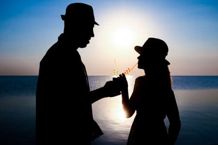 Happy couple drinking cocktail by the sea at sunset on travel silhouette in natureの写真素材