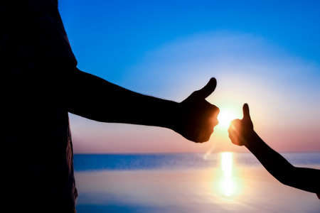 Hands of happy father and child by the sea on nature silhouette travelの写真素材