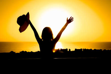Silhouette of a girl with a chair on a loggia balcony background. Happy woman with a hat in her arms while on vacation traveling.の写真素材