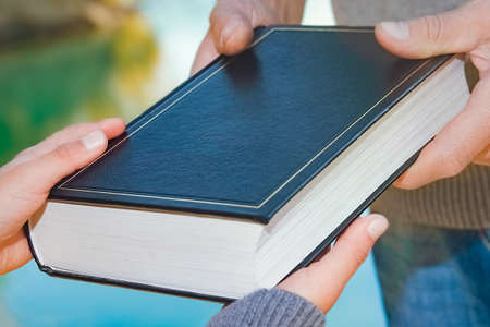 From hand to hand a parent passes a book to a child in a park outdoors travelの写真素材