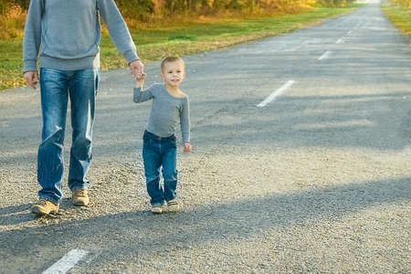 Happy parent with child are walking along the road in the park on nature travelの写真素材