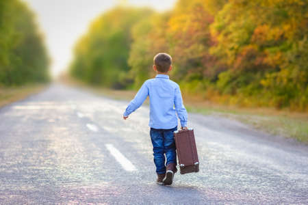 Happy child with a suitcase on the road in the park travelの写真素材