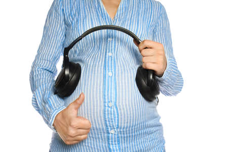 Happy pregnant girl with headphones in hands in hands on a white background. Positive music for the child.の写真素材