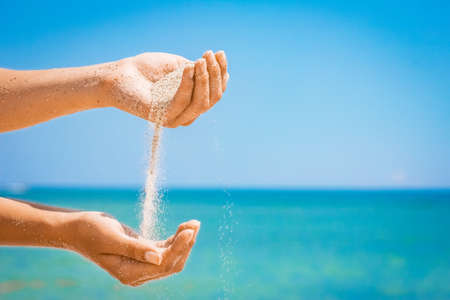 A Hands pour sand off the sea on nature on a journey. Vacations at sea sand time passes.の写真素材