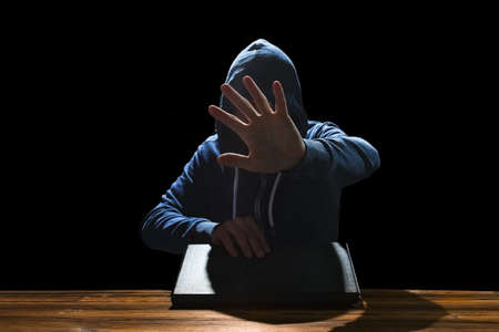 Hacker with computer man sitting at a table in a hood