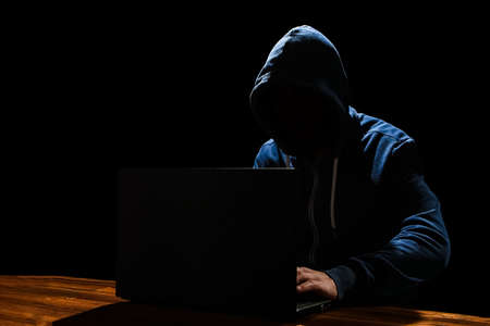 Hacker with laptop sits at a table and abstract binary code. Business life threat virtual programs.