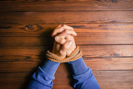 Hands tied with a rope life-threatening on a wooden background. Slavery in business is human abuse.の写真素材