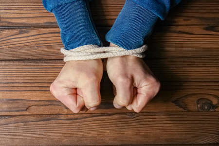 Hands tied with a rope life-threatening on a wooden background. Slavery in business is human abuse.