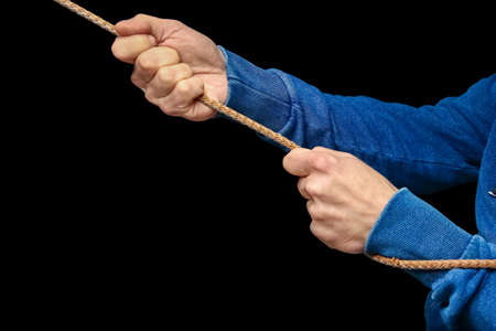 Hands with a rope on a black background. A man pulls a rope wrestling. Drag the business to your side.の写真素材