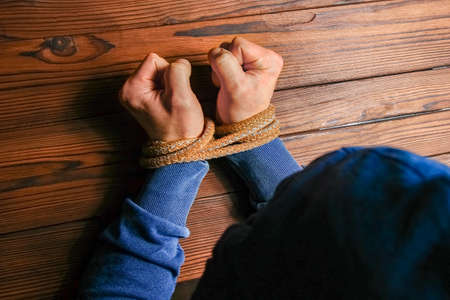Hands tied with a rope life-threatening on a wooden background. Slavery in business is human abuse.