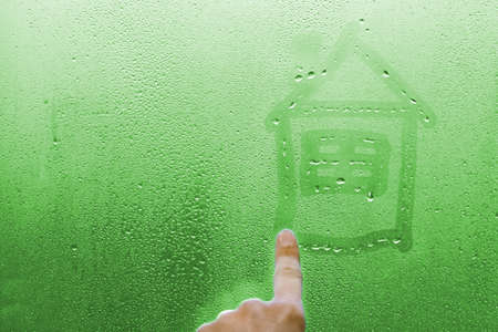 hand draws a house on a glass window with drops backgroundの写真素材