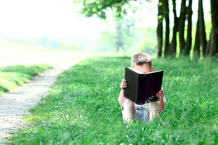 little happy boy reading the Bible book in natureの写真素材