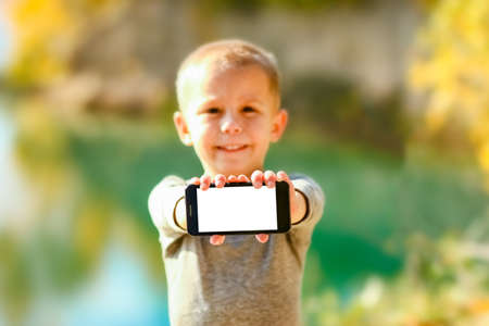Happy child with phone taking selfie in nature in the park travelの写真素材