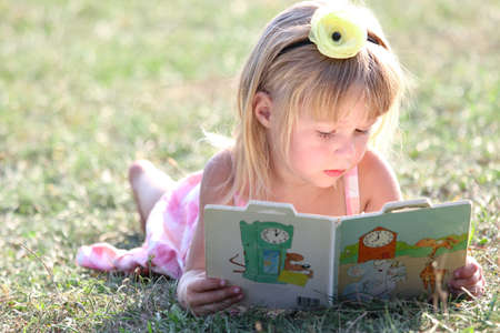happy child reading a book on nature in the park