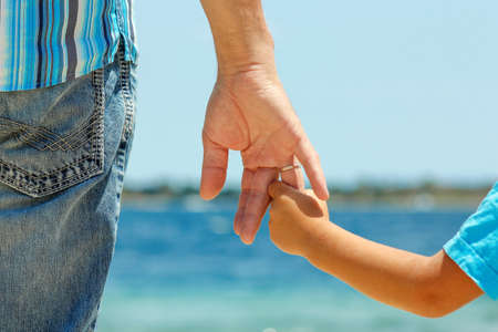 the parent holds the hand of a small child on seaの写真素材