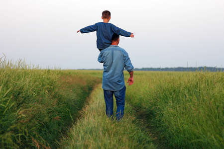 Happy child with parent on shoulders walk along the road in park backgroundの写真素材
