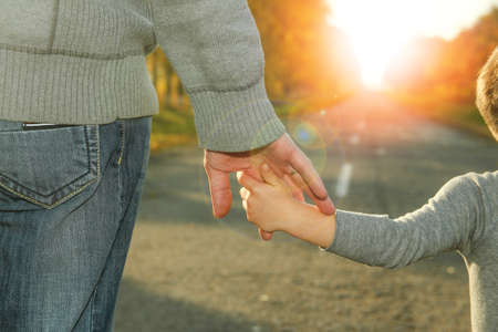 the parent holds the hand of a child walk near a roadの写真素材