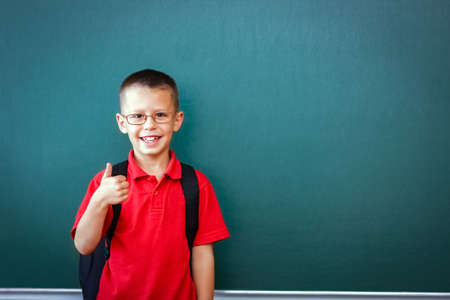 Happy child child standing at the blackboard with a school backpack wearing glasses