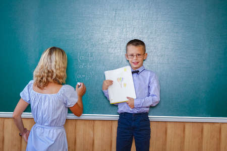 Happy child child standing at the blackboard with the school teacher at the lesson