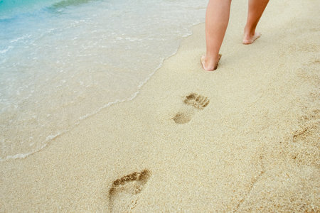 Beach travel - woman relaxing walking on a sandy beach leaving footprints in the sand. Close up detail of female feet on golden sand at a beach in Greece. Background.の写真素材