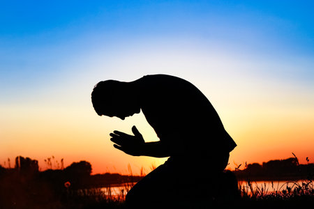 Silhouette of man praying at sunset backgroundの写真素材