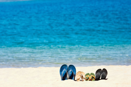 Slippers of the whole family in the sand by the sea on nature while traveling. Rest by the water on vacation with shoes.の写真素材