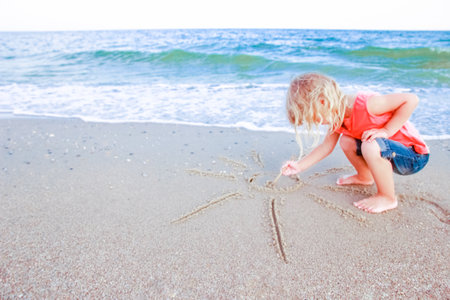 Happy child draw pictures in the sand of the sea in the summer on the natureの写真素材
