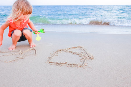 Happy child draw pictures in the sand of the sea in the summer on the natureの写真素材