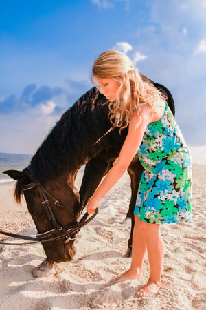 Happy pregnant woman with a horse on the beach in the summer on the natureの写真素材