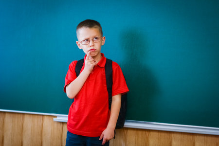 Happy child child standing at the blackboard with a school backpack wearing glassesの写真素材